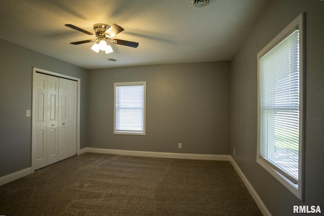 unfurnished bedroom with dark colored carpet, multiple windows, a closet, and ceiling fan