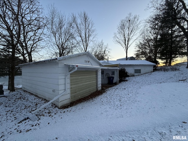 snow covered back of property featuring an attached garage