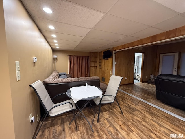 dining space with a drop ceiling, wooden walls, and hardwood / wood-style flooring