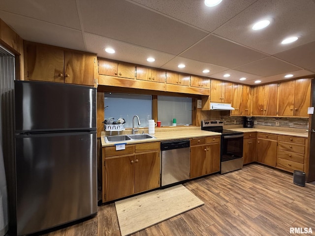 kitchen featuring stainless steel appliances, light countertops, brown cabinetry, a sink, and wood finished floors