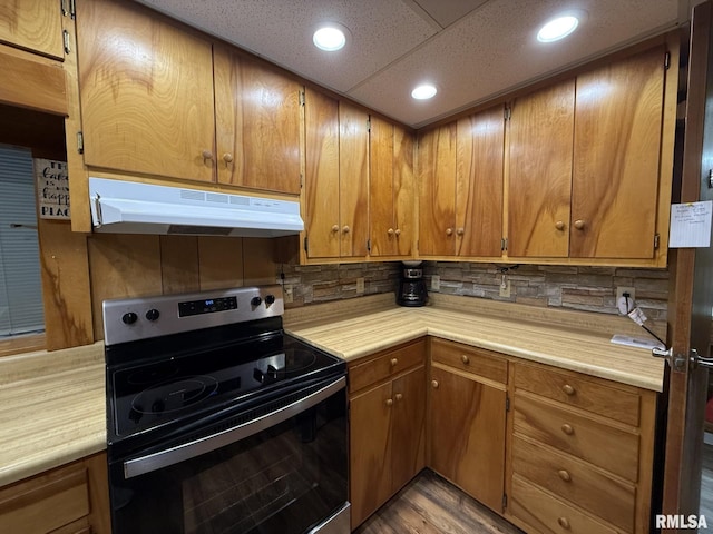 kitchen featuring light countertops, range with electric stovetop, brown cabinets, and under cabinet range hood