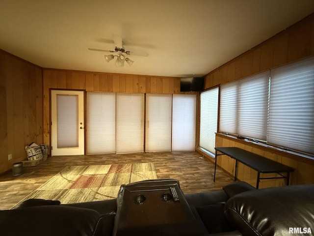 living area featuring a ceiling fan, wood walls, and wood finished floors