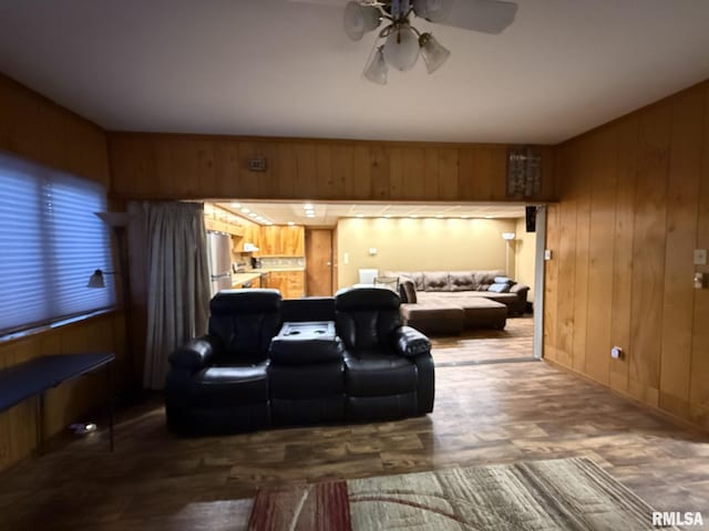 living area featuring dark wood-style floors, ceiling fan, and wood walls