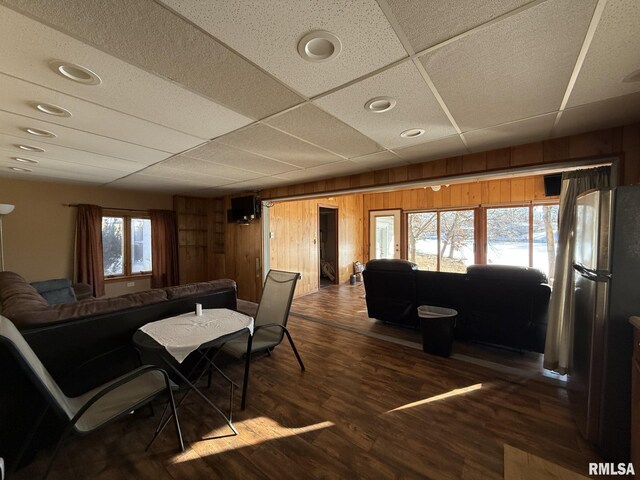 living room with ceiling fan, a paneled ceiling, wood walls, and hardwood / wood-style flooring