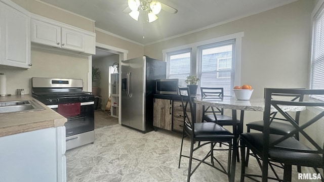 kitchen with sink, ceiling fan, stainless steel appliances, ornamental molding, and white cabinets