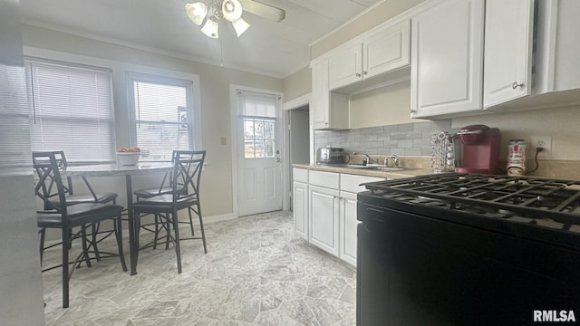 kitchen with black gas range oven, white cabinetry, sink, backsplash, and ornamental molding