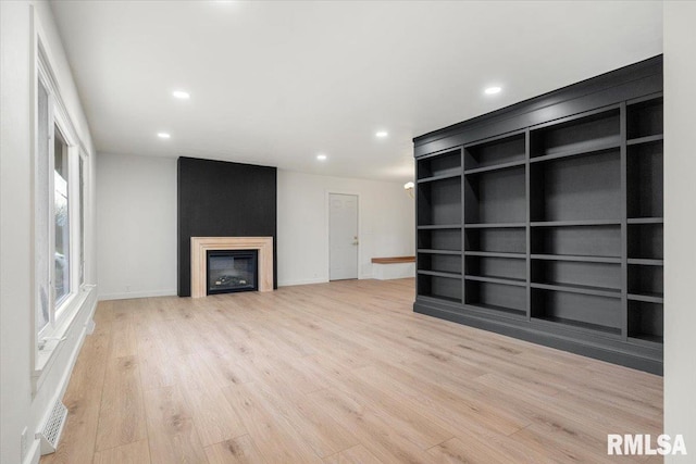 unfurnished living room with built in shelves, a large fireplace, and light hardwood / wood-style floors