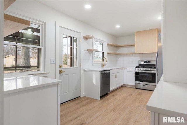 kitchen featuring backsplash, white cabinets, sink, light hardwood / wood-style flooring, and stainless steel appliances