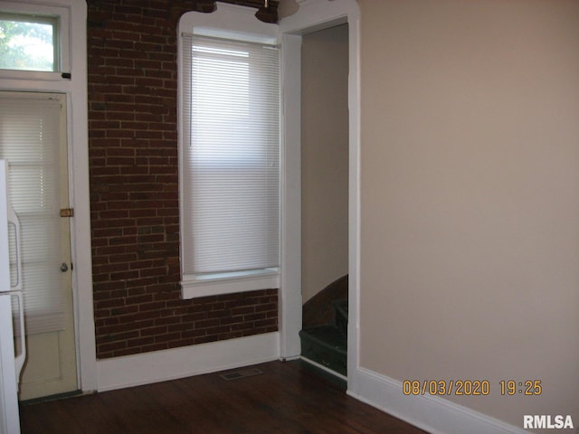 empty room featuring dark wood-type flooring and brick wall