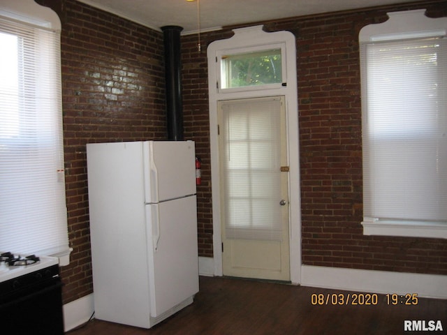 kitchen with dark hardwood / wood-style flooring, white appliances, and brick wall