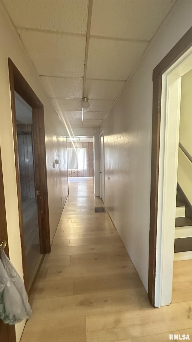 hall with light wood-type flooring and a paneled ceiling