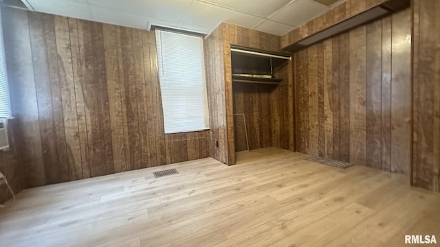 interior space with light wood-type flooring, a paneled ceiling, and wood walls