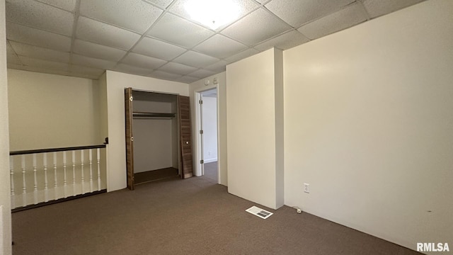 unfurnished bedroom with carpet flooring, a drop ceiling, and a closet