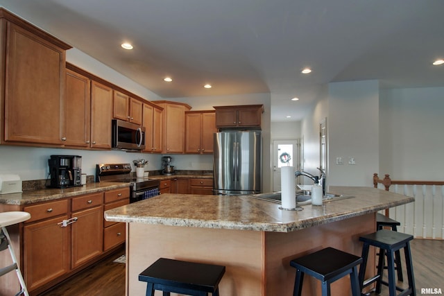 kitchen featuring a kitchen breakfast bar, a kitchen island with sink, dark hardwood / wood-style flooring, and appliances with stainless steel finishes