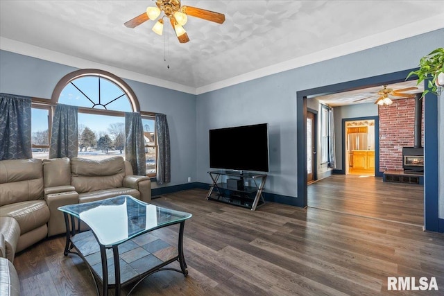 living room featuring a wood stove, ceiling fan, dark hardwood / wood-style flooring, and ornamental molding