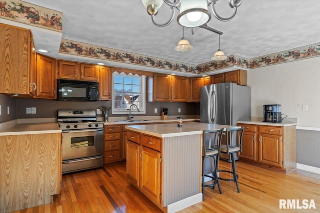 kitchen featuring appliances with stainless steel finishes, sink, a center island with sink, light hardwood / wood-style flooring, and decorative light fixtures