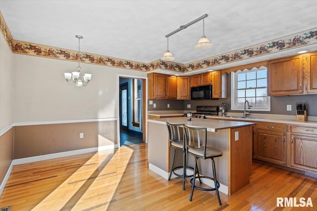 kitchen featuring sink, a notable chandelier, pendant lighting, a kitchen island with sink, and black appliances