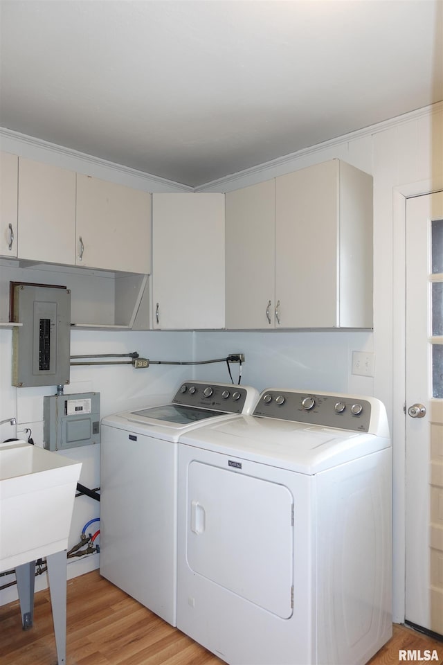 clothes washing area featuring cabinets, ornamental molding, light hardwood / wood-style flooring, washing machine and dryer, and electric panel