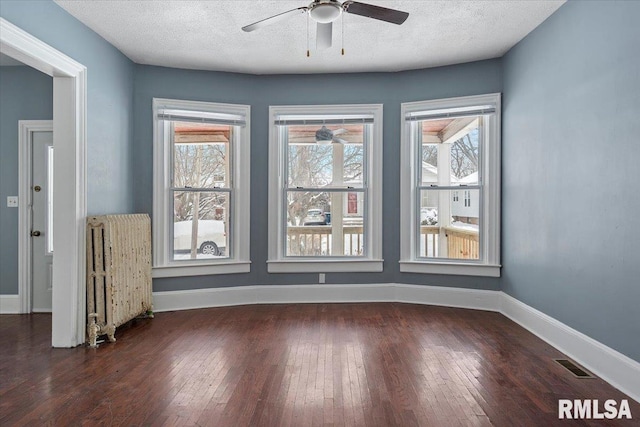 spare room featuring dark hardwood / wood-style flooring, ceiling fan, radiator heating unit, and a textured ceiling