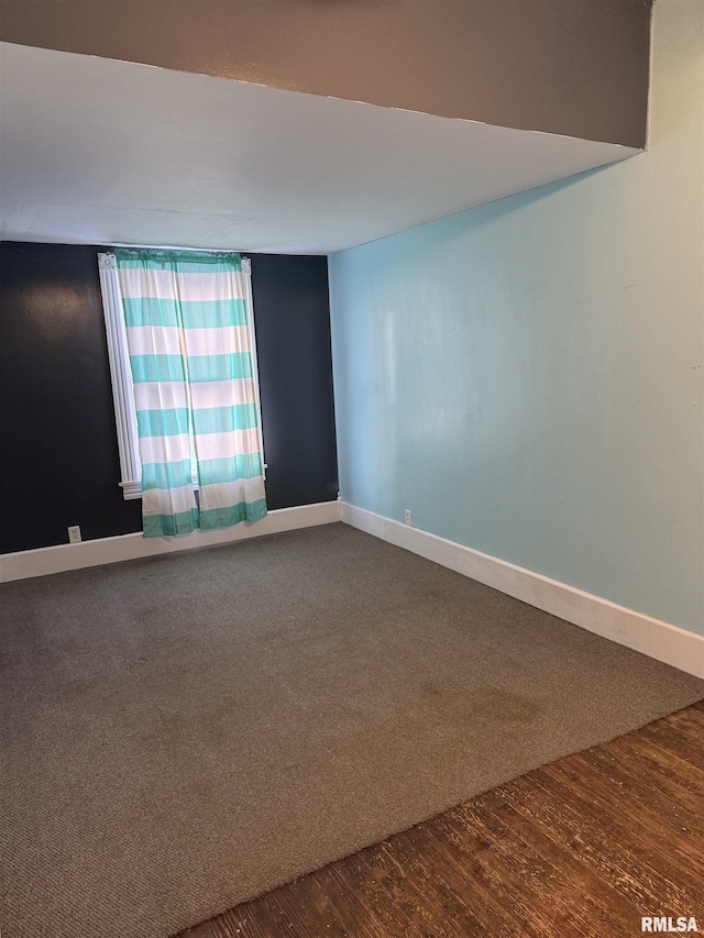 empty room with dark colored carpet, baseboards, and dark wood-style flooring