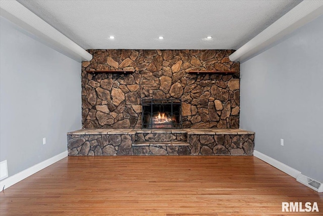 unfurnished living room featuring hardwood / wood-style flooring, a stone fireplace, and a textured ceiling