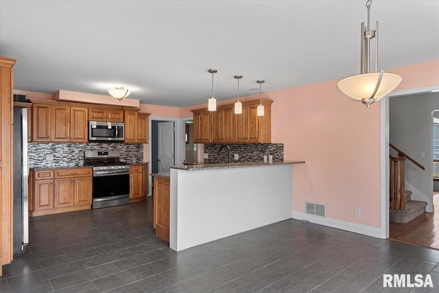 kitchen featuring kitchen peninsula, dark stone countertops, pendant lighting, decorative backsplash, and appliances with stainless steel finishes