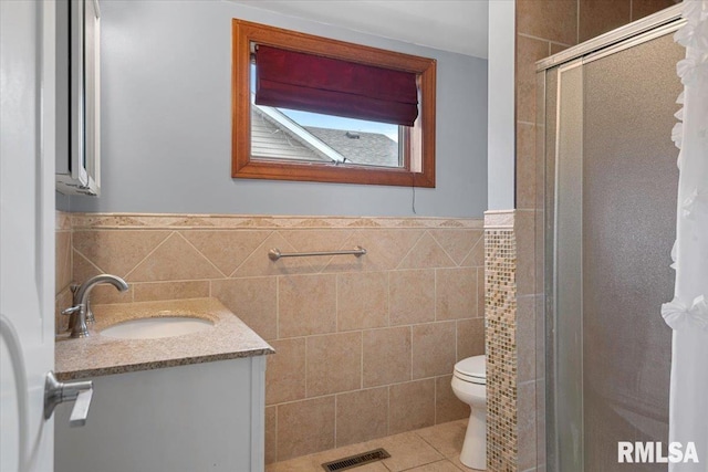 bathroom featuring tile patterned flooring, vanity, a shower with door, and tile walls