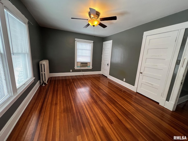 empty room with dark hardwood / wood-style floors, ceiling fan, radiator, and cooling unit