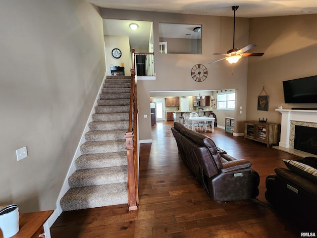 living room featuring ceiling fan, dark wood-type flooring, a premium fireplace, and a high ceiling