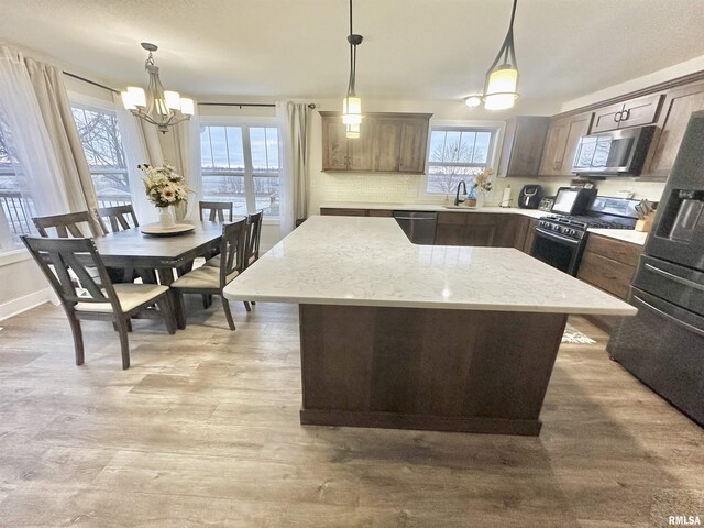 kitchen featuring pendant lighting, tasteful backsplash, a notable chandelier, a kitchen island, and stainless steel appliances