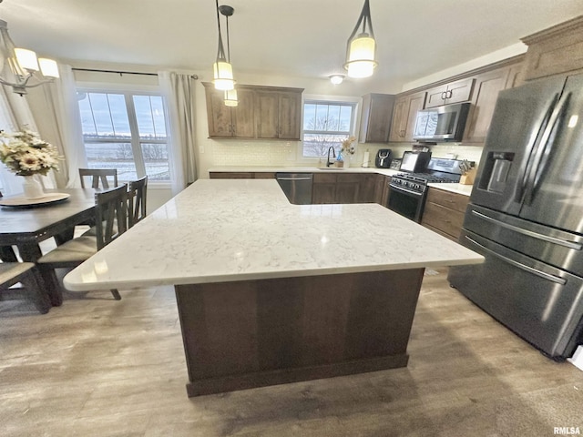 kitchen featuring light stone countertops, appliances with stainless steel finishes, sink, decorative light fixtures, and a kitchen island