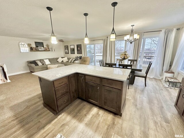 kitchen with light stone counters, dark brown cabinets, hanging light fixtures, and plenty of natural light