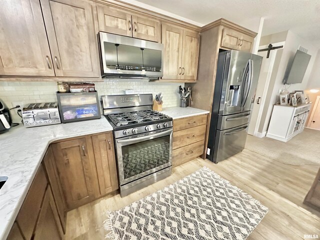 kitchen featuring a barn door, light wood-type flooring, appliances with stainless steel finishes, tasteful backsplash, and light stone counters