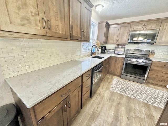 kitchen with light stone countertops, sink, stainless steel appliances, tasteful backsplash, and light hardwood / wood-style flooring