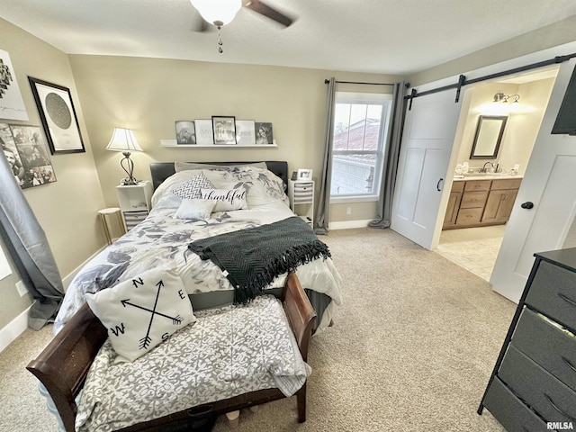 carpeted bedroom featuring a barn door, ensuite bath, ceiling fan, and sink