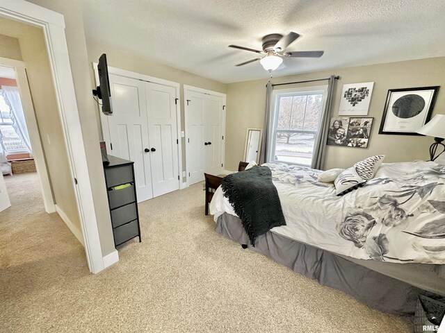 carpeted bedroom featuring a textured ceiling, ceiling fan, and multiple closets