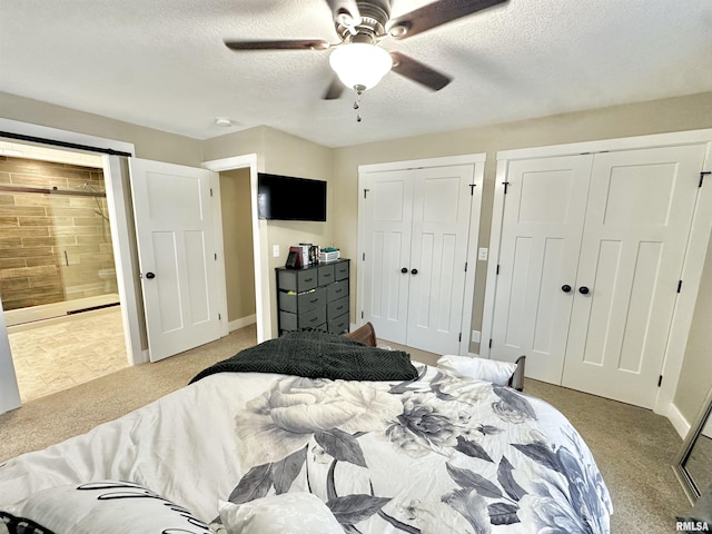 carpeted bedroom featuring a textured ceiling, ensuite bath, ceiling fan, and two closets