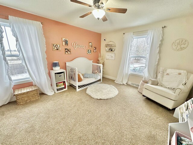 bedroom with a textured ceiling, carpet floors, a nursery area, and ceiling fan