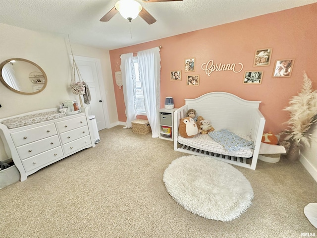 bedroom featuring light carpet, a textured ceiling, a crib, and ceiling fan