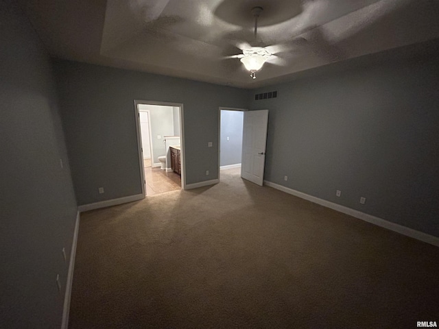 unfurnished bedroom with ceiling fan, light colored carpet, ensuite bath, and a tray ceiling