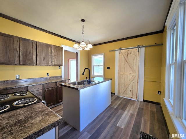 kitchen featuring a kitchen island with sink, crown molding, sink, a barn door, and decorative light fixtures