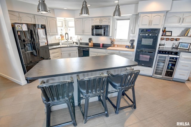 kitchen featuring black appliances, decorative light fixtures, white cabinets, wine cooler, and a breakfast bar area