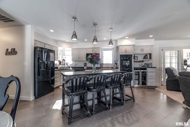 kitchen with a kitchen bar, a wealth of natural light, beverage cooler, black appliances, and decorative light fixtures