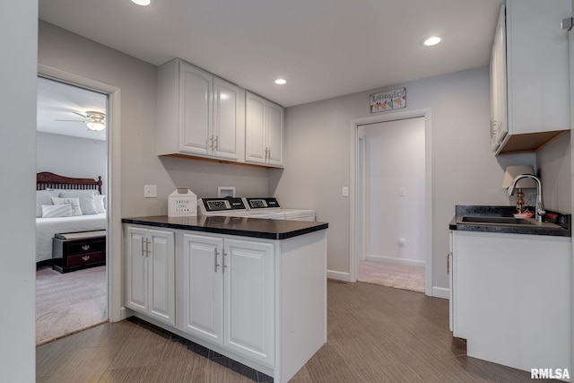 kitchen featuring washing machine and clothes dryer, white cabinetry, sink, ceiling fan, and light carpet