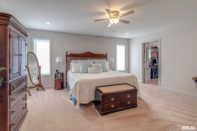 bedroom featuring a spacious closet, a closet, ceiling fan, and light carpet