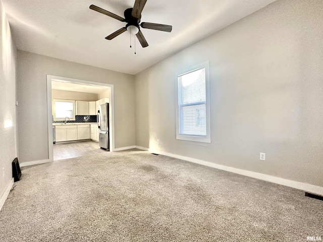 unfurnished living room featuring ceiling fan, sink, and light carpet