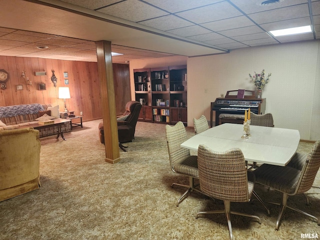 carpeted dining space featuring a drop ceiling and wooden walls