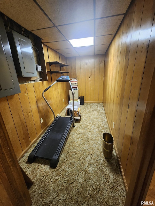 workout area with dark colored carpet, a paneled ceiling, electric panel, and wooden walls