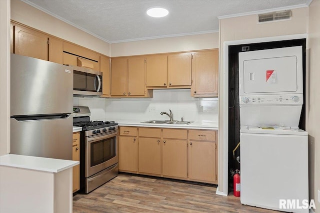 kitchen with sink, ornamental molding, stacked washer and clothes dryer, stainless steel appliances, and light hardwood / wood-style flooring