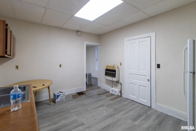 interior space featuring a paneled ceiling, visible vents, light wood-style floors, baseboards, and heating unit